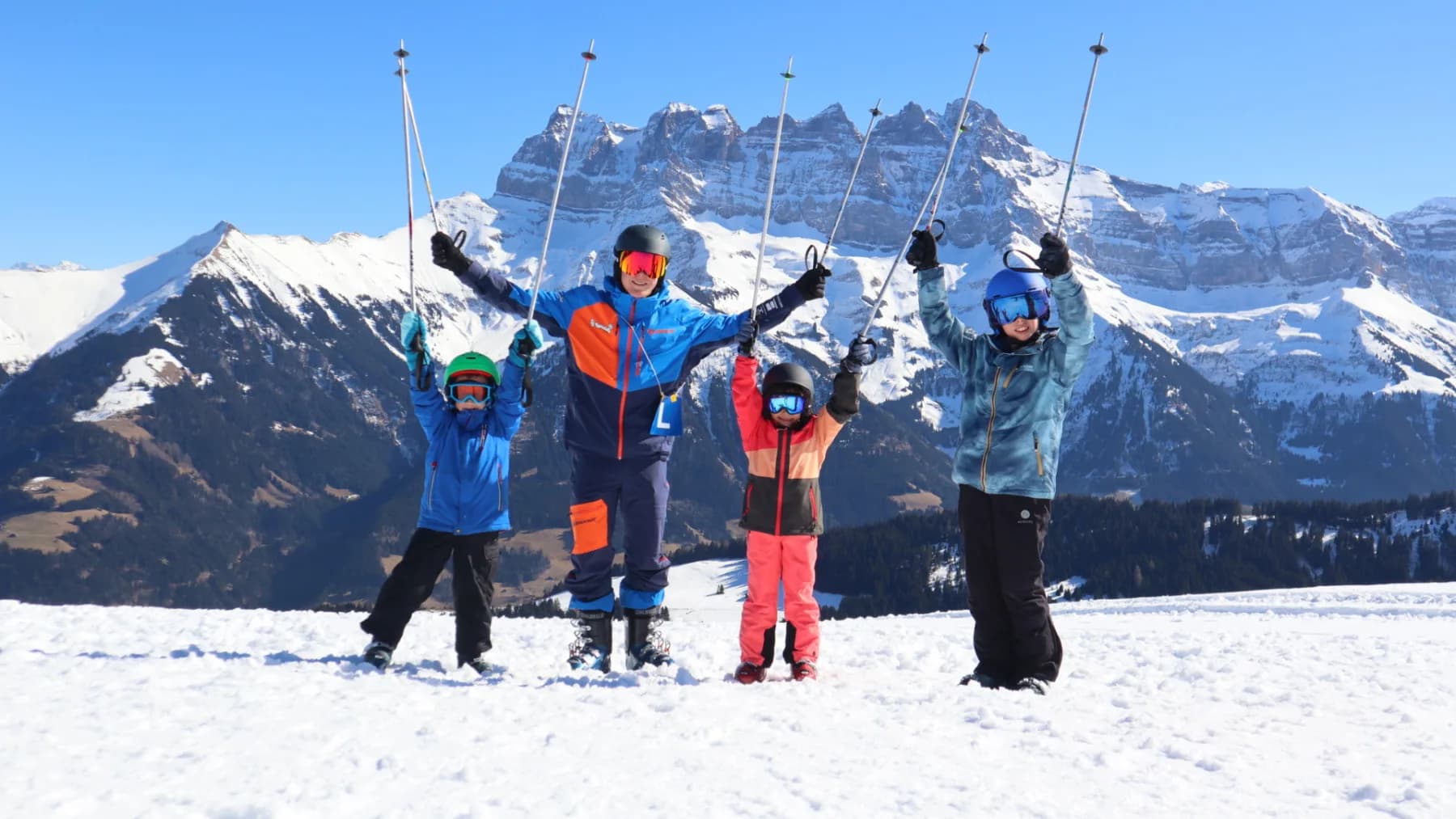 Quatre skieurs de l'OJ Vuadens, bâtons levés, devant les Dents du Midi